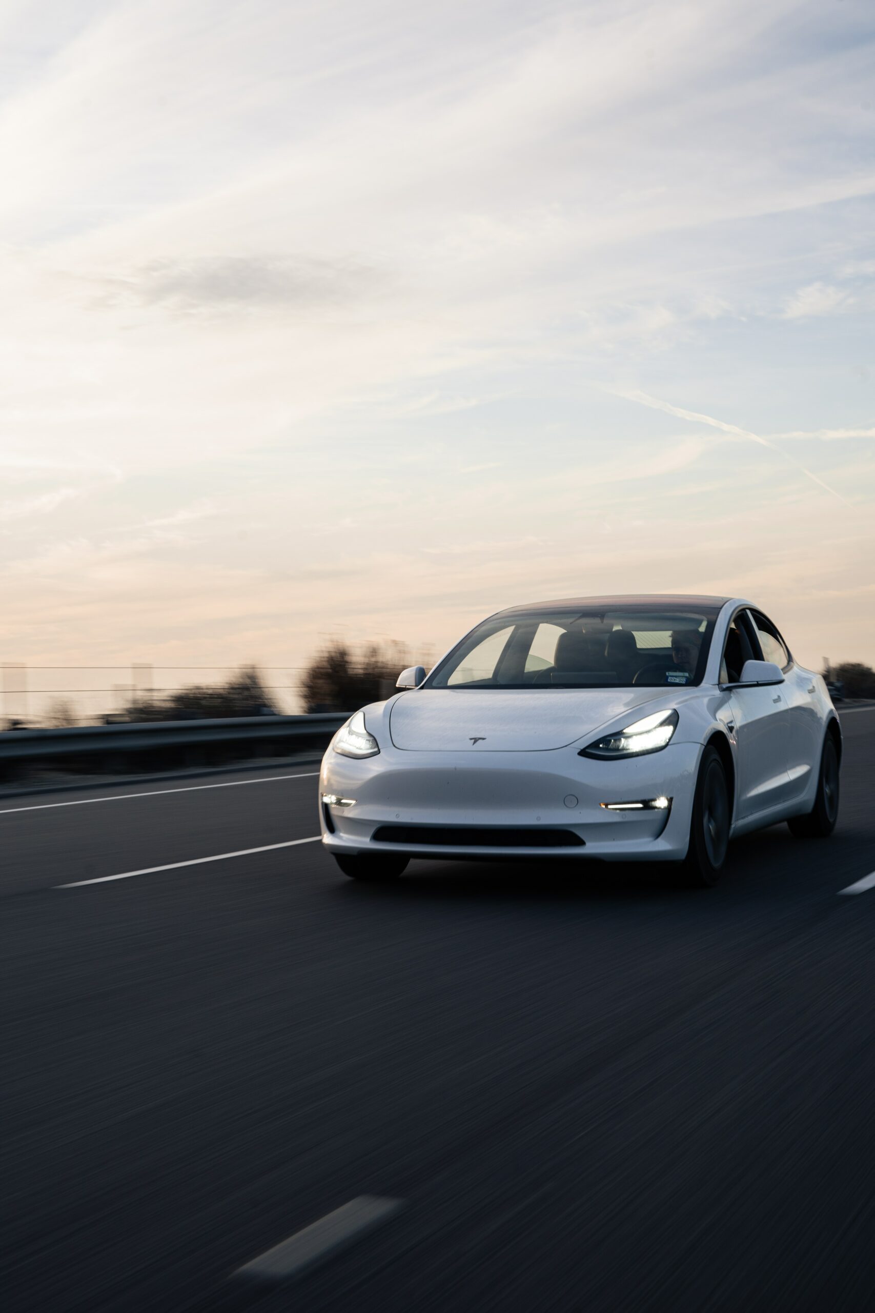 White Tesla Model 3 driving down the road with dusk in the background